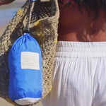 Alaya Beach Company packable beach blanket folding into pouch by the ocean.