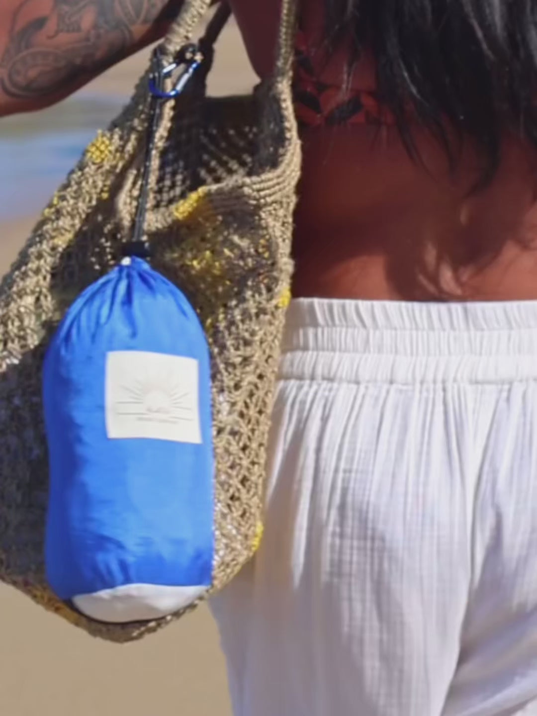 Alaya Beach Company packable beach blanket folding into pouch by the ocean.